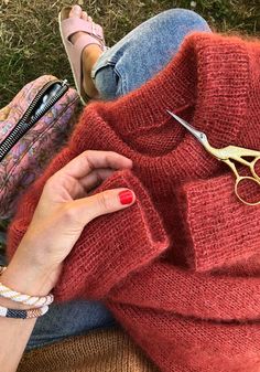 a woman is sitting on the grass with her purse and pair of scissors next to her