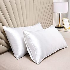 two white pillows sitting on top of a bed next to a nightstand with a lamp