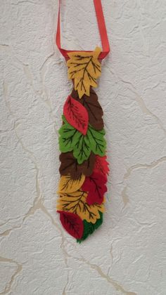 a tie made out of leaves hanging on a wall with a red ribbon around it