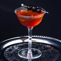 an alcoholic cocktail with olives in a martini glass on a black tray, ready to be served