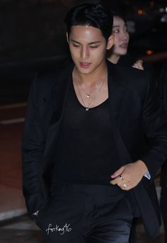 the young man is walking down the street in his black suit and silver bracelets