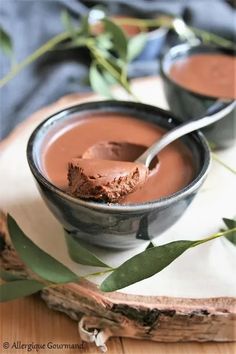 two bowls filled with chocolate pudding sitting on top of a wooden table next to leaves