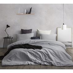 an unmade bed with grey sheets and pillows