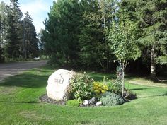 a large rock sitting in the middle of a lush green field next to a forest