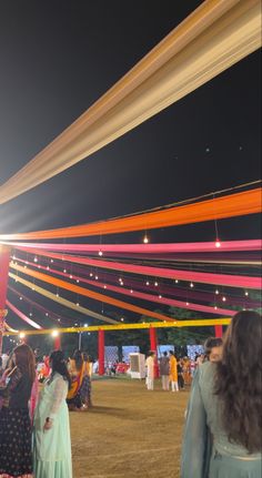 people are standing under colorful ribbons at an outdoor event with lights on the ceiling and in the background