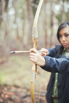 a woman is aiming an arrow in the woods while wearing a jacket and holding it with both hands