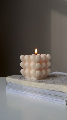 a white candle sitting on top of a book next to a lit candle in the shape of hearts