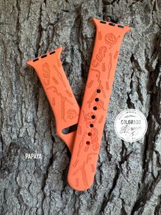 two orange watch bands are sitting on a tree trunk with the words papapaa printed on them