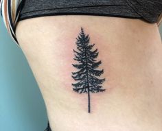 a small pine tree tattoo on the side of a woman's ribcage