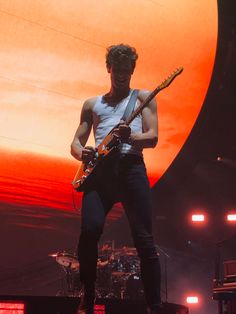 a man standing on top of a stage with a guitar in his hand and an orange sun behind him