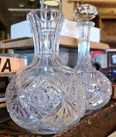 two clear glass decanters sitting on top of a wooden table next to books