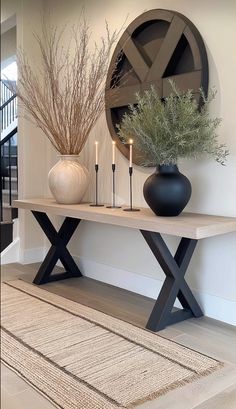 two vases with plants and candles on a table next to a round wall decoration