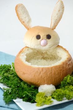 a bread bun with a bunny face sticking out of it sitting on top of lettuce