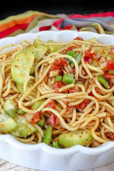 a white bowl filled with pasta and vegetables on top of a table next to a fork