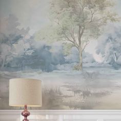 a lamp sitting on top of a table next to a wall with a tree painted on it