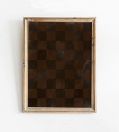 a brown and black checkered wall hanging on a white wall next to a wooden frame