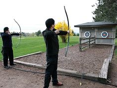 two young men are practicing archery in the park