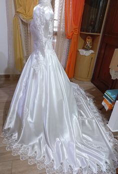 a white wedding dress on display in front of a window with curtains and other items behind it