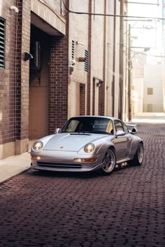 a silver sports car parked on the side of a brick road next to a building