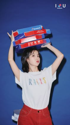 a young woman is holding three boxes on her head while standing against a blue background