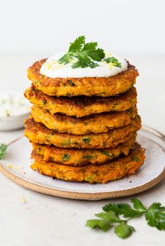 a stack of carrot fritters topped with sour cream and cilantro leaves