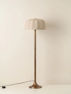 a floor lamp with a white shade on it and a black cord plugged in