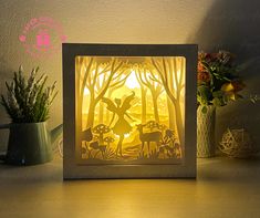 an illuminated paper cut scene with deer and mushrooms in the woods at night, on a table next to potted plants