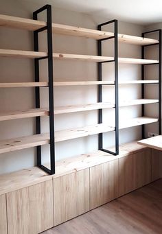 an empty room with wooden shelves and black metal brackets on the wall, along with wood flooring