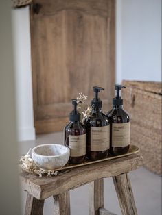 three bottles of soap sitting on top of a wooden table next to a basket with flowers