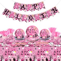 a pink table topped with plates and cups filled with cake next to a banner that says happy halloween