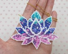 a hand holding a piece of beaded art with a flower on it's side