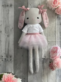 a stuffed rabbit in a pink tutu and dress with flowers around it on a wooden surface