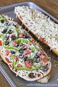 two slices of pizza with cheese, olives, and peppers on a baking tray