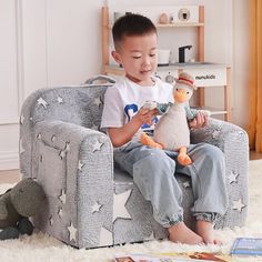 a young boy sitting in a chair holding a stuffed animal and looking at his phone