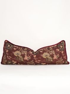 a red pillow with flowers on it sitting on a white surface in front of a wall