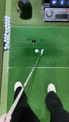 a person standing on top of a green field with a golf ball and club in hand