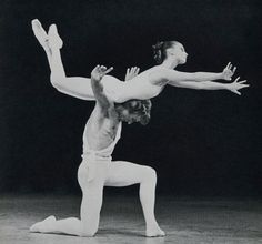 two dancers in white pose for the camera, one holding his leg up and the other leaning forward