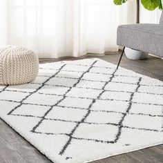 a white and black rug in a living room next to a gray couch with a plant on it