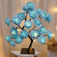 there is a small tree with blue roses on it and lights in the back ground