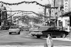 an old black and white photo of cars driving down the street in front of stores