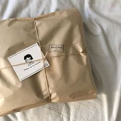 a brown wrapped gift box with a tag on it sitting on a white bed sheet