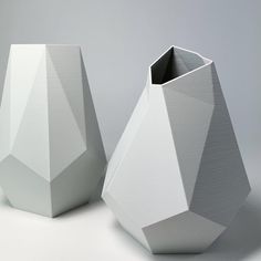 two white vases sitting next to each other on a gray surface with no one in it