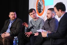 three men sitting in chairs talking to each other at a panel discussion with one man holding out his hand