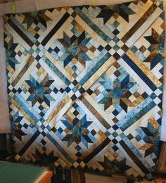 a quilt hanging on the wall next to a book shelf with books and other items