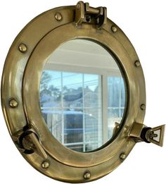 an old brass porthole mirror on a white wall with a window in the background