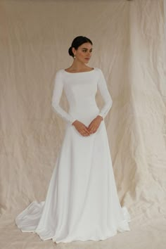 This unique wedding dress, made from luxurious crepe, is an ideal minimalistic elegance. With long sleeves and an A-line silhouette, this floor-length gown with a long train is perfect for winter weddings, including Christmas or civil ceremonies.  The modest design features a flattering boat neckline and a high back, creating a timeless and graceful look. Bridal buttons flow down the back and extend to the end of the train, adding a touch of classic beauty, long sleeves are also complemented wit A Line Long Sleeve Wedding Dress, Classy Simple Wedding Dress, Long Sleeve Wedding Dress Winter, Christmas Wedding Dress, Bridal Buttons, Modest Bridal Dresses, Wedding Dress Winter, Modest Wedding Dresses With Sleeves, Gowns Vintage