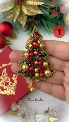 a hand holding a christmas tree brooch on it's finger next to a red box