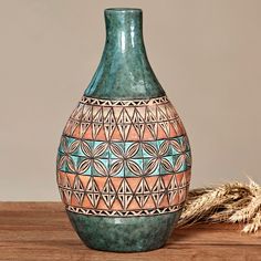 a green vase sitting on top of a wooden table next to a dried plant in front of it