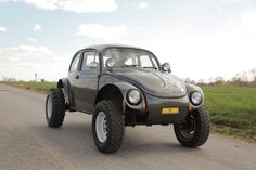 an old beetle car is parked on the side of the road in front of some grass