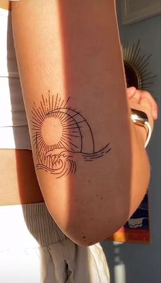 a woman's arm with a tattoo on it and the sun in the background